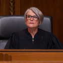 Image of a female judge wearing a black judicial robe seated on the wooden bench in the courtroom of the Thomas J. Moyer Ohio Judicial Center.