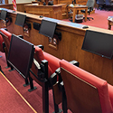 Image showing an empty jury box in a courtroom. Several monitors are mounted in front of jurors' seats.