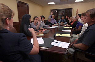 Image of people sitting around a table in a jury deliberation room.