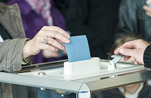 Image of a closeup of a woman's hand placing a ballot into a ballot box (Thinkstock)