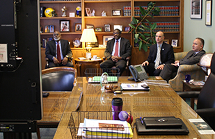 Image of four men dressed in suits sitting in a conference room facing a large monitor Image of four men dressed in suits sitting in a conference room facing a large monitor