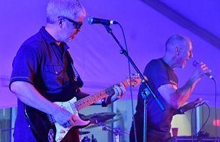 Image of a man playing an electric guitar standing next to another man singing into a microphone