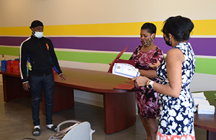 Image of a man and two women standing in a brightly painted room - one woman is holding a graduation certificate