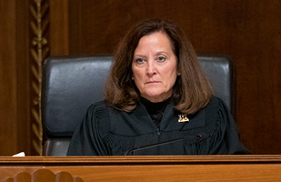 Image of a woman sitting on a court bench listening to the court case