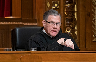 Image of a man in his judicial robe sitting on a court bench talking to a party in the case he's hearing