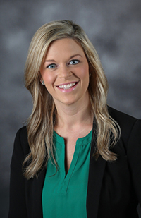 Image of a woman with long, blond hair wearing a green top and a black suit jacket