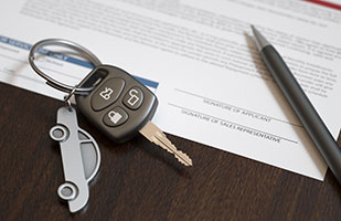 Image of a silver car-shaped keychain holding a single car key, sitting on top of a document along with an ink pen (Thinkstock)