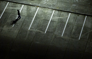 Image of a person wearing a hoodie walking in an empty parking lot at night (jaap-willem/iStock)