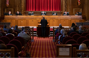 Image of an attorney standing at a lecturn addressing the Chief Justice and Justices sitting on the bench in the courtroom of the Thomas J. Moyer Ohio Judicial Center