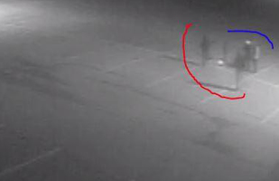 Grainy image from a surveillance camera of people standing in en empty parking lot at night