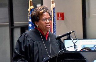 Image of a female judge wearing a black judicial robe speaking from a podium.