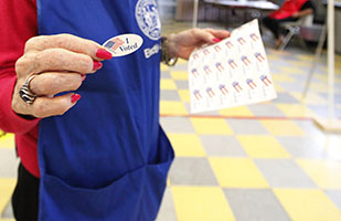 Image of an election volunteer holding up a sticker that says, 'I Voted.'