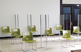 Image of several chairs located 6 feet apart and separated by plexiglass barriers