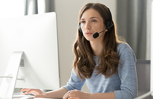 Image of a woman wearing a headset microphone sitting in front of a computer (iStock/fizkes)