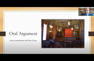 Image of a slide from a Powerpoint presentation showing the courtroom of the Thomas J. Moyer Ohio Judicial Center with a smaller image of a man speaking in the upper right-hand corner