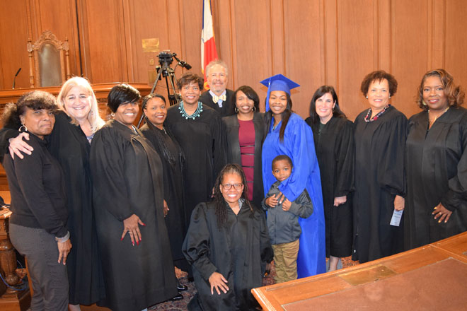 Image of several men and women, many wearing black judicial robes, standing side-by-side in a courtroom