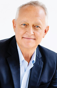 Image of grey-haired, blue-eyed Caucasian man wearing a blue blazer and blue button-up shirt.