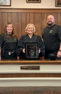 Image of female judge in a judicial robe holding an award. On either side of her is a man and a woman.