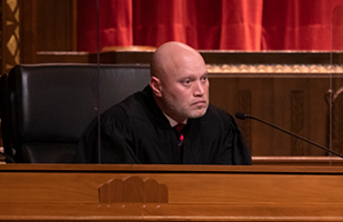 Image of a male judge wearing a black judicial robe in a courtroom