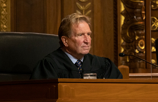 Man in black judicial robe sitting behind bench.