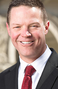 Image of a man wearing a dark grey suit and red tie.