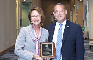 Woman in professional attire holding a plaque next to a man in a suit and tie.