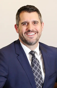 Image of a man wearing a blue suit, white dress shirt, and blue plaid tie