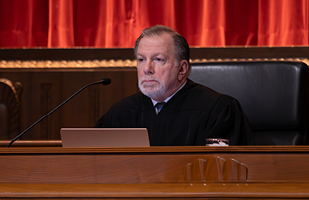 Image of a male judge wearing a black judicial robe seated at the bench in the courtroom of the Thomas J. Moyer Ohio Judicial Center.