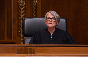 Image of a female judge wearing a black judicial robe seated on the wooden bench in the courtroom of the Thomas J. Moyer Ohio Judicial Center.