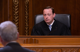 Image of a male judge wearing a black judicial robe seated at the wooden judicial bench in the Thomas J. Moyer Ohio Judicial Center.