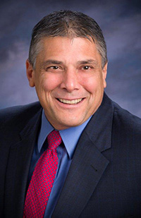 Image of a man wearing a dark blue suit and red and blue tie.