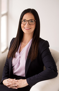 Image of a woman with long, dark hair and glasses wearing a pink blouse and dark jacket.