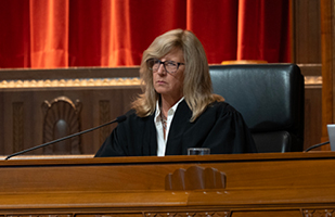 A woman wearing a black judicial robe is seated at a wooden bench in the courtroom of the Thomas J. Moyer Ohio Judicial Center.
