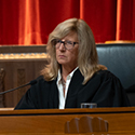 A woman wearing a black judicial robe is seated at a wooden bench in the courtroom of the Thomas J. Moyer Ohio Judicial Center.