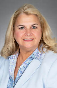 A woman wearing a light blue suit and paisley shirt.