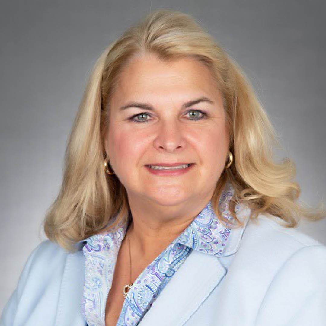 A woman wearing a light blue suit and paisley shirt.