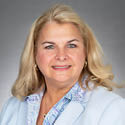 A woman wearing a light blue suit and paisley shirt.