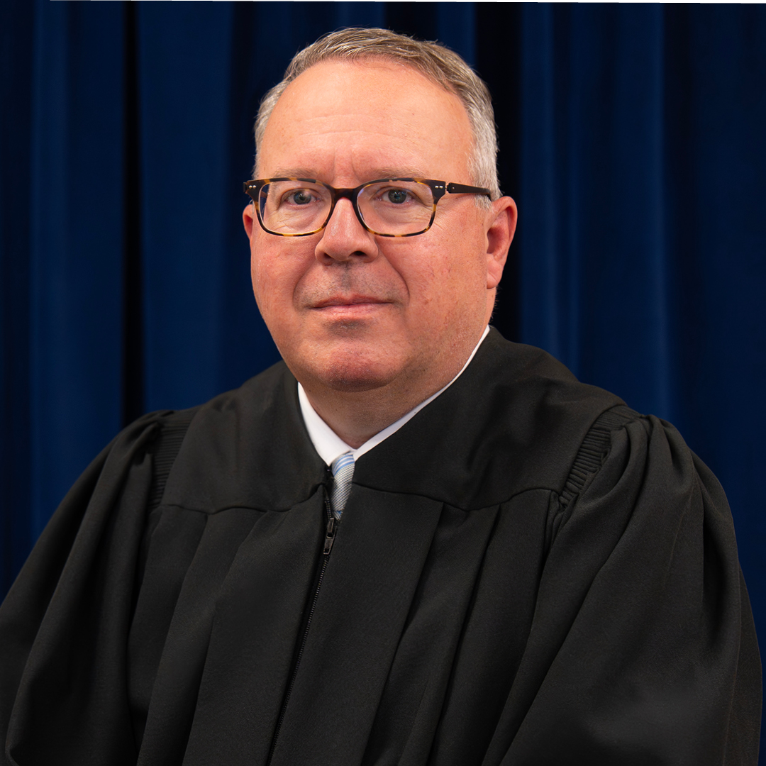 A man wearing a judicial robe in front of a blue background