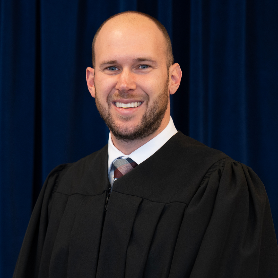 a man wearing a judicial robe standing infront of a blue background