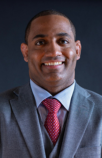 A man wearing a grey three-piece suit, white dress shirt, and red tie.