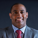A man wearing a grey three-piece suit, white dress shirt, and red tie.