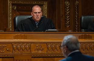 A man in judicial robe sitting at a wooden bench in a courtroom