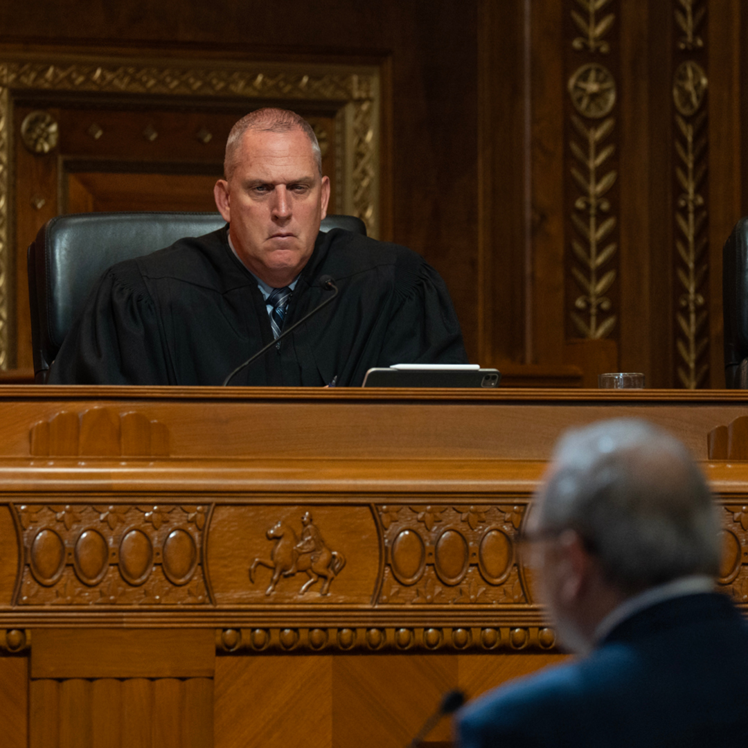 A man in judicial robe sitting at a wooden bench in a courtroom