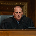 A man in judicial robe sitting at a wooden bench in a courtroom