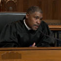 A male judge wearing a black judicial robe seated at a wooden bench in the courtroom of the Thomas J. Moyer Ohio Judicial Center.