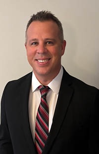 A man wearing a dark suit jacket, white dress shirt, and red stripe pattern tie.