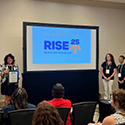 Four women standing by a projector screen holding an award