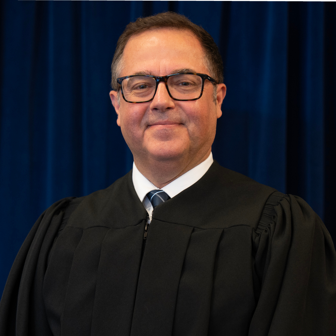 Three judges wearing black robes stand against a blue curtain backdrop. Each person is centered in their own segment of the arrangement.