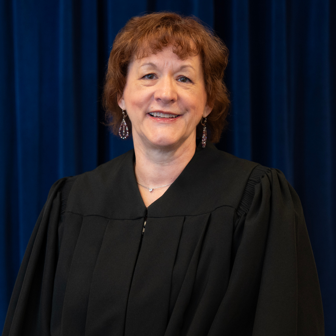 Three judges wearing black robes stand against a blue curtain backdrop. Each person is centered in their own segment of the arrangement.