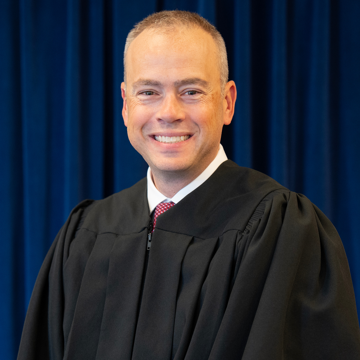 A judge in a black robe smiling.